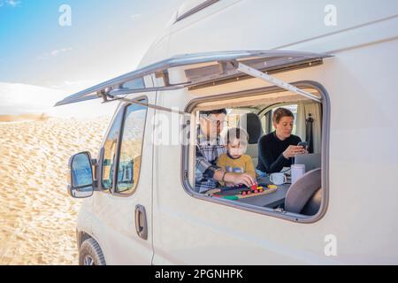 Son playing with father in motor home at desert on sunny day Stock Photo
