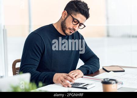 Man with calculator sitting at desk in office Stock Photo