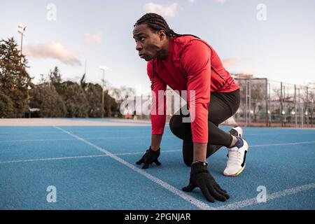 Determined athlete in starting position preparing to run on track Stock Photo