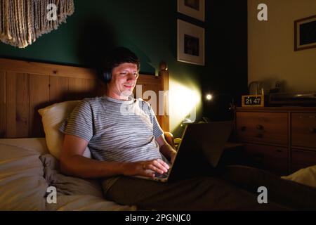 Man using laptop sitting on bed at home Stock Photo