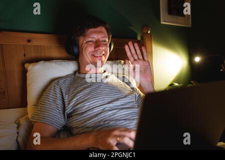 Smiling man waving on video call in bedroom at home Stock Photo