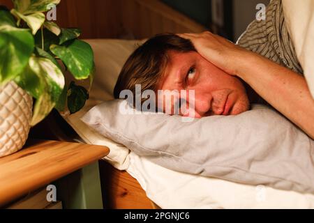 Man covering ears lying down on bed at home Stock Photo