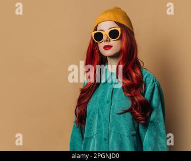 Redhead woman wearing knit hat and sunglasses against brown background Stock Photo