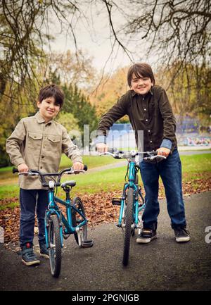 Smiling brothers with bicycles standing on footpath at park Stock Photo