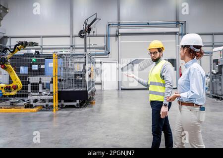 Engineers wearing hardhats discussing in factory Stock Photo