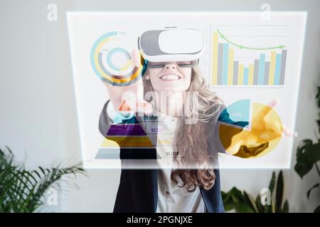 Happy businesswoman wearing VR goggles and examining graphs and pie charts Stock Photo