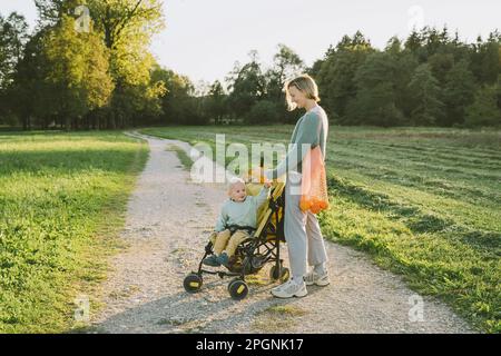 Woman with son sitting in baby stroller on footpath Stock Photo