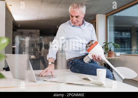 Engineer working on laptop holding wind turbine rotor at desk in office Stock Photo