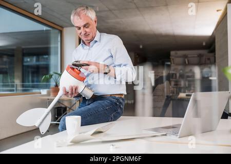 Senior engineer examining wind turbine rotor sitting on desk at office Stock Photo