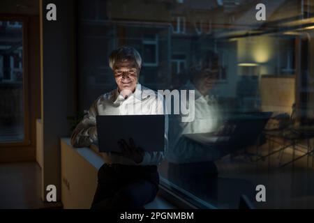 Smiling businessman working late on laptop at office Stock Photo