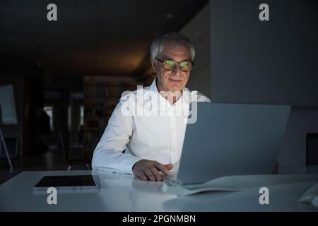 Elderly businessman using laptop sitting at desk in office Stock Photo