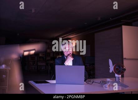 Businessman with hand on chin working late at office Stock Photo