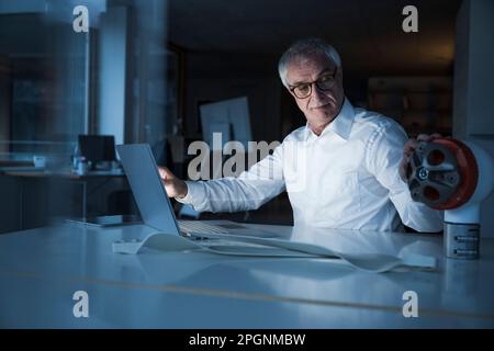 Senior engineer examining rotor sitting with laptop at desk in office Stock Photo