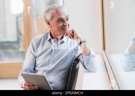 Thoughtful businessman with hand on chin looking out of window at workplace Stock Photo