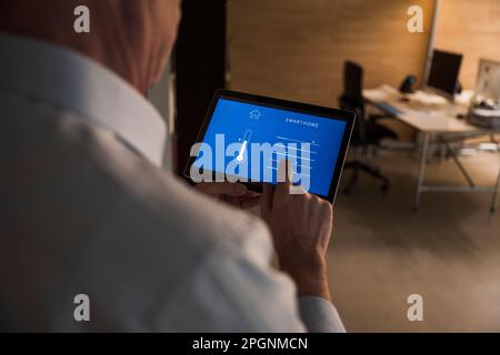 Senior businessman adjusting temperature through home automation app on tablet PC at office Stock Photo