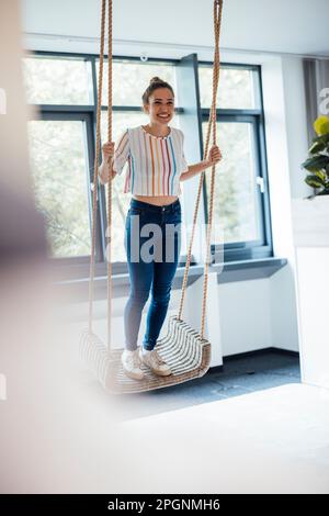 Happy businesswoman standing on swing in office Stock Photo