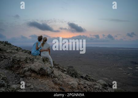 Couple looking at sunset sitting on mountain Stock Photo