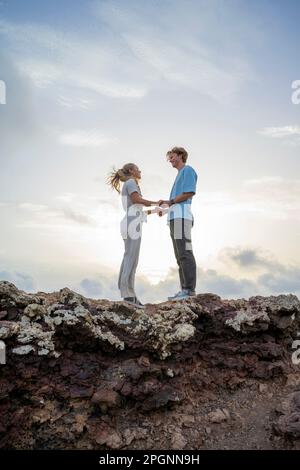 Young couple standing on cliff holding hands Stock Photo