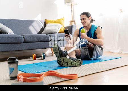 Smiling young man with disability using smart phone sitting at home Stock Photo