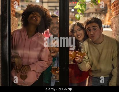 Young friends holding drinks having fun seen through glass Stock Photo