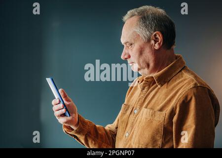 Senior man using smart phone by wall Stock Photo