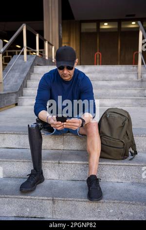 Mature man with disability using smart phone sitting on steps Stock Photo
