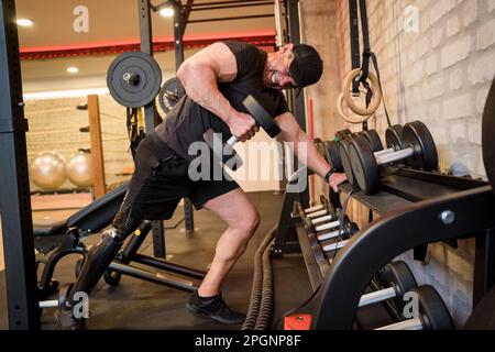 Mature man with prosthetic leg lifting weights in gym Stock Photo