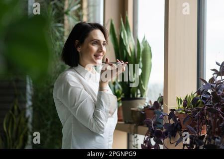 Happy woman talking on mobile phone standing by window Stock Photo