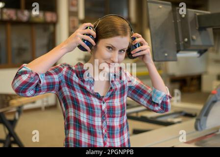 Smiling craftswoman wearing ear protectors in woodshop Stock Photo