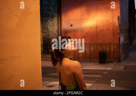 Thoughtful young woman looking up by wall at night Stock Photo