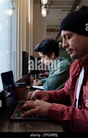 Freelancer working on laptop with brother in cafe Stock Photo