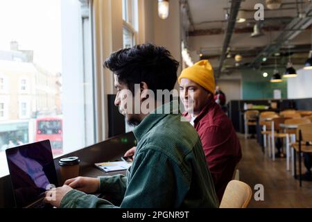 Young freelancer working on laptop with brother in cafe Stock Photo