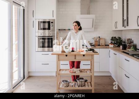 Thoughtful woman leaning on table in kitchen at home Stock Photo