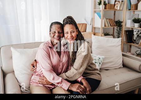 Smiling mother and daughter sitting on sofa at home Stock Photo