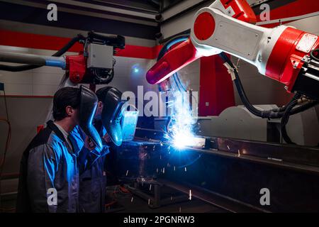 Engineers wearing protective workwear by robotic arm welding in factory Stock Photo