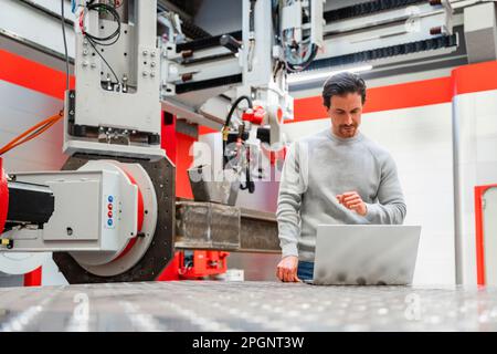 Technician working on laptop in robot factory Stock Photo