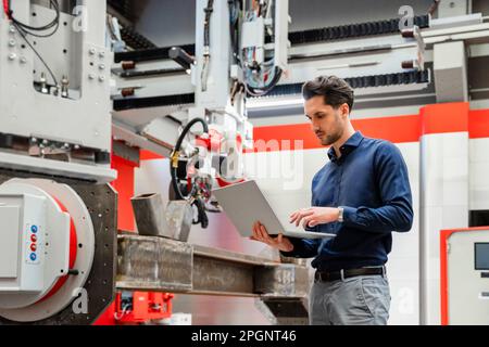 Engineer working on laptop in robot factory Stock Photo