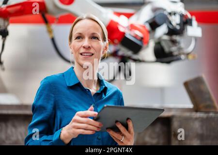 Contemplative engineer holding tablet PC in robot factory Stock Photo