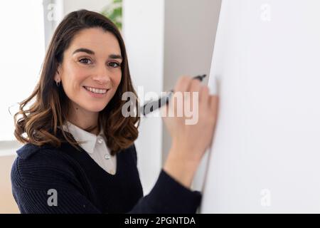 Happy businesswoman with felt tip pen writing on flipchart Stock Photo