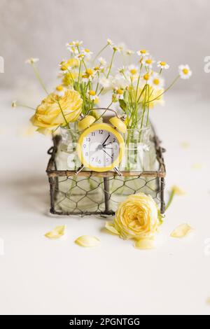 Yellow and white flowers in vase with alarm clock on table Stock Photo