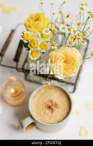 Cup of coffee by yellow and white flowers on table Stock Photo