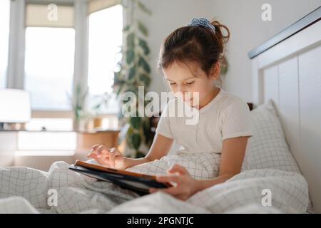 Girl using tablet PC sitting in bedroom Stock Photo