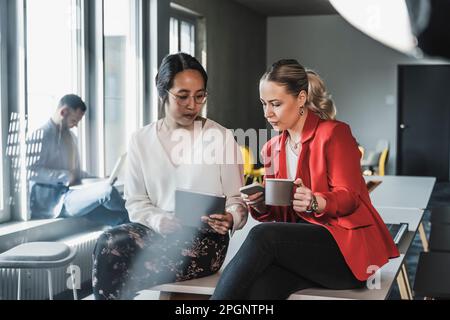 Businesswomen using wireless technologies sitting at desk in office Stock Photo