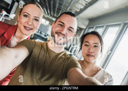 Smiling businessman taking selfie with colleagues at office Stock Photo