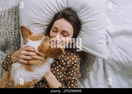 Mature woman with eyes closed lying on bed with dog at home Stock Photo