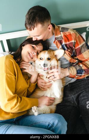 Couple embracing and playing with Pembroke Welsh Corgi sitting at home Stock Photo