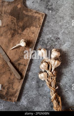 Raw garlic, cutting board and kitchen knife lying on gray surface Stock Photo
