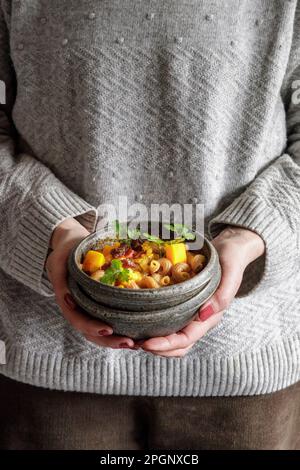Midsection of woman holding bowl of North African stew with pumpkin, chickpeas, lentils, dates and cilantro Stock Photo