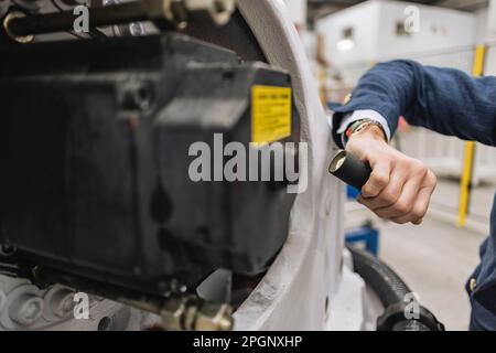 Hand of engineer holding flashlight examining machine part in factory Stock Photo
