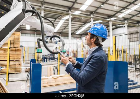 Engineer examining robotic arm using tablet computer in factory Stock Photo